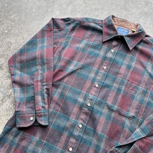 May include: A long-sleeved, button-down shirt with a plaid pattern in shades of teal, burgundy, and gray. The shirt has a collared neckline, a chest pocket, and the brand name "Pendleton" on a tag.