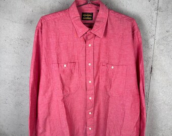 May include: A long-sleeve button-down shirt in a vibrant pink hue, featuring a classic collar, two chest pockets with button closures, and a full-length front button placket. The garment is displayed on a metal hanger against a textured wall.