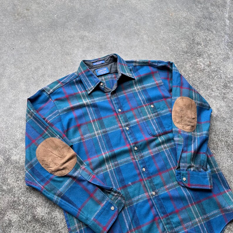 Op de afbeelding: Blauw geruit overhemd met bruine elleboogstukken. Het overhemd heeft een klassiek ruitpatroon in blauw, groen en rood. De elleboogstukken hebben een contrasterende bruine kleur. Het heeft een kraag en manchetten met knopen.