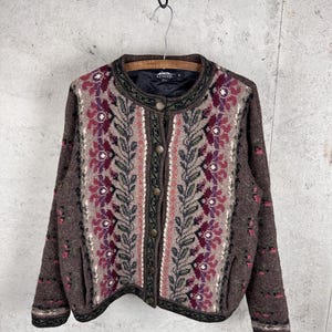 May include: A brown knit cardigan featuring a vertical pattern of dark green leaves and burgundy floral motifs. The garment has a round neckline, long sleeves, and a front button closure with metallic buttons. The interior is lined with black fabric.