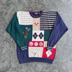 May include: A patchwork golf-themed sweater with a variety of patterns and colors. The sweater features argyle, stripes, and golf club graphics. The sweater has a navy blue ribbed hem and cuffs, with a red and navy blue neckline.