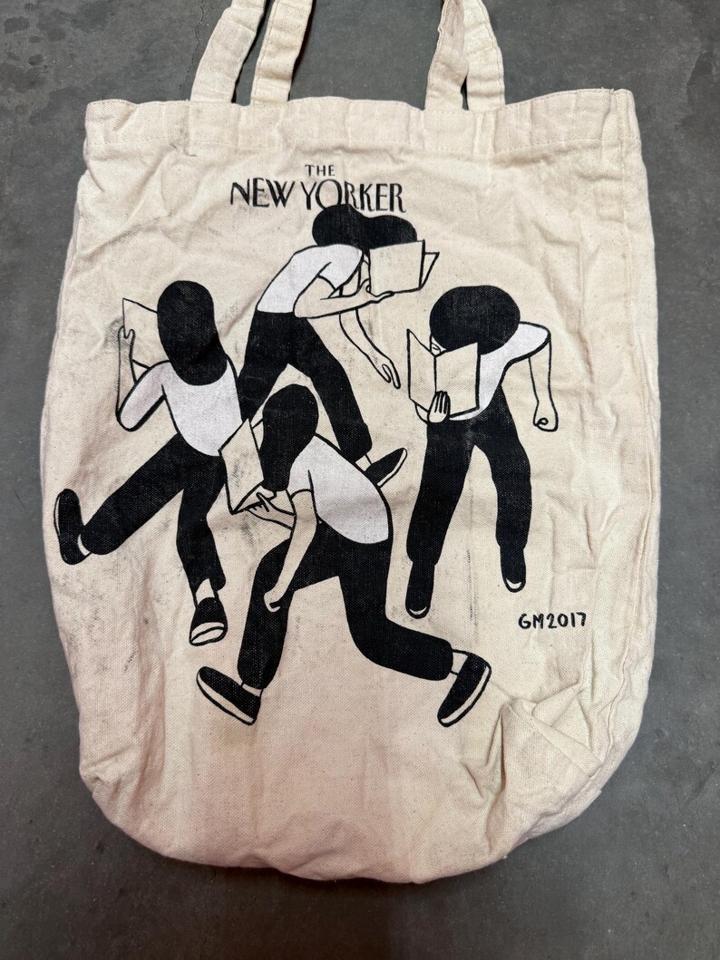 May include: Off-white canvas tote bag featuring the text "The New Yorker" above a black and white illustration of figures reading books. The illustration includes four figures in motion, with the artist's signature "GM2017" at the bottom.