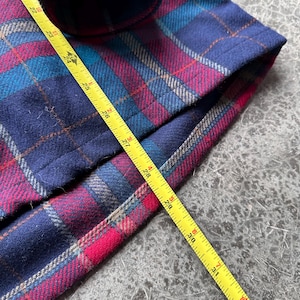 K&ouml;nnte beinhalten: Nahaufnahme eines karierten Stoffes in Marineblau, T&uuml;rkis und Magenta. Ein gelbes Ma&szlig;band liegt auf dem Stoff und zeigt Messungen bis zu 79 cm an.