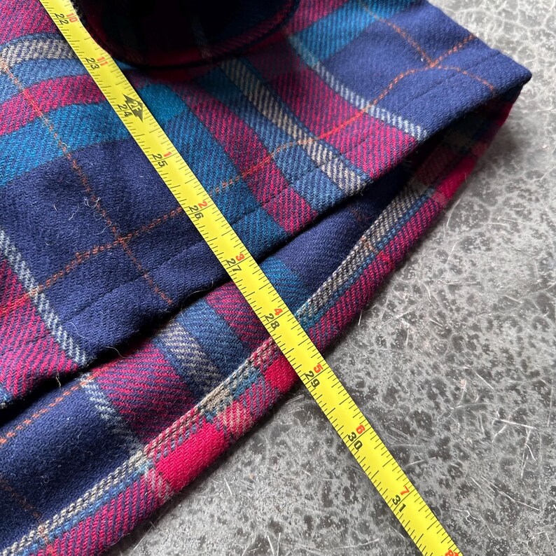 K&ouml;nnte beinhalten: Nahaufnahme eines karierten Stoffes in Marineblau, T&uuml;rkis und Magenta. Ein gelbes Ma&szlig;band liegt auf dem Stoff und zeigt Messungen bis zu 79 cm an.