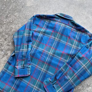 Op de afbeelding: Een blauw geruit flanellen overhemd met lange mouwen. Het overhemd heeft een klassiek ruitpatroon in tinten blauw, groen, rood en wit. Het overhemd is gemaakt van een zacht, comfortabel materiaal.