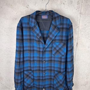 May include: A long-sleeve button-up jacket featuring a blue and black plaid pattern. The jacket includes a notched collar, a single chest pocket on the left side, two lower front pockets, and a Pendleton brand label inside the neck area.