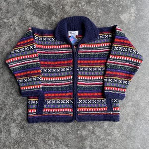 May include: A navy blue, zip-up sweater with a colorful, geometric pattern. The sweater features horizontal stripes in red, green, purple, and white. It has a collared neckline and two pockets. The sweater is made of a knitted material.