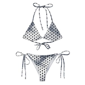 Puede incluir: Un bikini blanco y gris con un estampado de rayos negros. La parte superior es de estilo triangular con tirantes ajustables y lazos en la parte posterior. La parte inferior es de estilo atrevido con lazos ajustables a los lados.