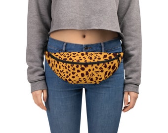 May include: A yellow fanny pack with a brown leopard print pattern. The bag has a black zipper and strap. The person in the image is wearing blue jeans and a gray cropped sweatshirt.