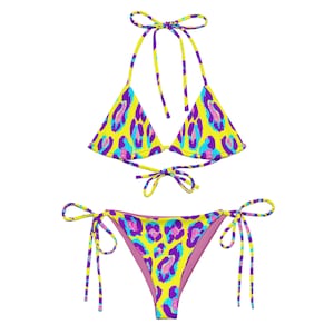 Op de afbeelding: Een gele bikini met een paarse en blauwe luipaardprint. De top is een driehoek-stijl met verstelbare bandjes en strikjes aan de achterkant. De onderkant is een cheeky stijl met strikjes aan de zijkanten.