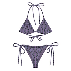May include: A two-piece bikini set in a purple snakeskin pattern. The top is a triangle style with halter ties, and the bottoms are a classic tie-side design. The fabric has a textured appearance, and the overall style is suitable for swimwear.
