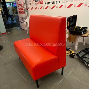 Puede incluir: Un asiento de cabina de cuero rojo con patas de metal negro. La cabina está en un restaurante con una pared blanca detrás. La pared tiene texto negro y rojo que dice "Feast Cheat Day Shake Things Up A Little Bit Legen-Dairy".