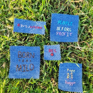 May include: Five denim patches with embroidered messages. The patches are on a green grassy background. The messages are "Revolution", "Born to be Mild", "People Before Profit", "Rec", and "Tree Hugger".