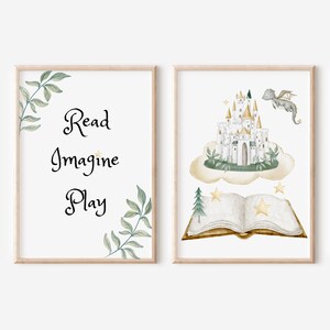 May include: Two framed watercolor prints. One reads "Read Imagine Play" with leafy accents. The other depicts a castle on a cloud, a dragon, an open book, and stars. The prints have a light wood frame.