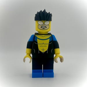 May include: A custom Lego minifigure of the character Invincible. The figure has a yellow head with white eyes and a black hair piece. The torso is yellow with a blue and black suit design. The legs are blue, and the hands are yellow.