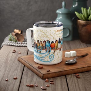 May include: White ceramic mug featuring a colourful design of birds perched on a branch. The mug has a blue and white swirling pattern and a gold background. The birds are a variety of colours, including blue, green, yellow, and red.