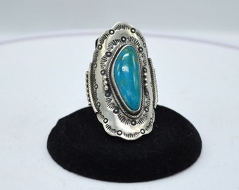 May include: A silver ring with an oval turquoise stone. The ring has a decorative border with a rope-like design and small silver beads. The turquoise stone is a vibrant blue color.