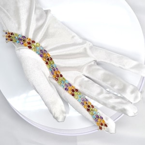 May include: A multi-colored gemstone bracelet featuring oval-cut stones in shades of red, yellow, green, blue, and purple. The bracelet is displayed on a white surface.