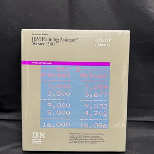 Può includere: Scatola sigillata del software IBM Planning Assistant Versione 2.00, con floppy disk da 3,5" e 5,25". La scatola ha uno sfondo beige con testo blu e rosa, inclusi dati finanziari. Il logo IBM è visibile.