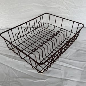 May include: A rectangular, dark brown wire dish rack with a grid base and vertical dividers for plates. The rack has curved accents and is designed to hold dishes for drying. The wire frame is sturdy and the design is simple.