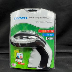 May include: A black and gray Dymo Embossing Labelmaker Organizer Xpress label maker with a white label tape. The label maker has a black handle and a white button. The packaging is green and white with the words "Office", "Hobby", and "Home" on it.