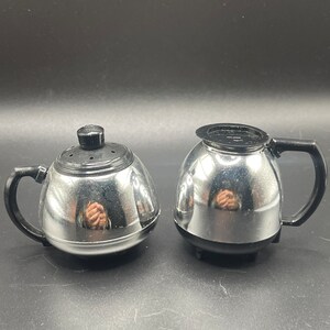 May include: A set of two silver and black salt and pepper shakers shaped like coffee pots.