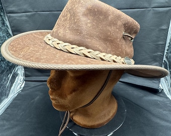 May include: A brown leather cowboy hat with a braided leather band and a brown leather chin strap.