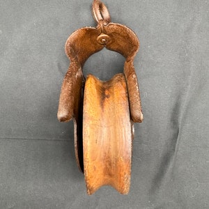 May include: A vintage wooden pulley with a metal frame. The pulley is brown and the frame is rusty.
