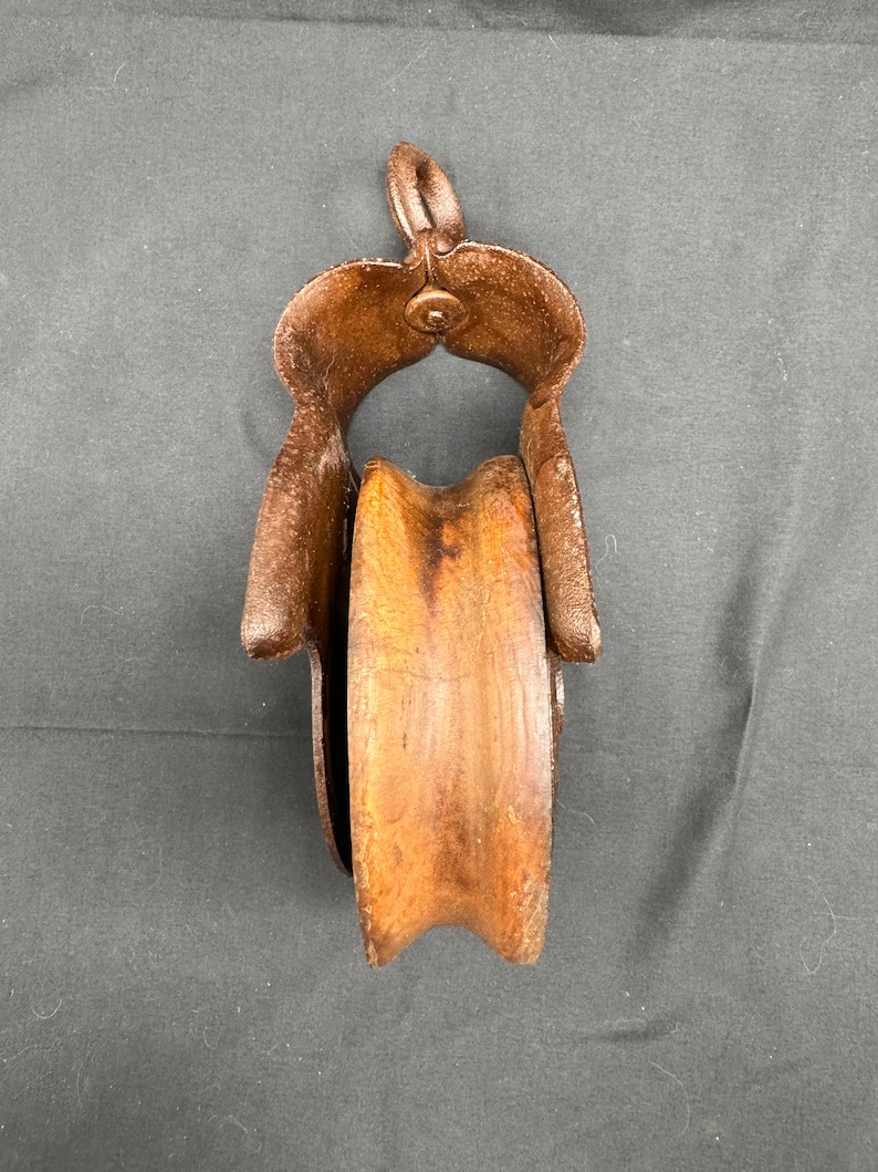 May include: A vintage wooden pulley with a metal frame. The pulley is brown and the frame is rusty.