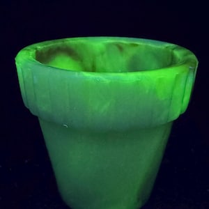 Puede incluir: Una maceta verde brillante con una forma clásica. La maceta tiene una superficie ligeramente texturizada y un borde superior acanalado. El color vibrante sugiere que puede estar hecha de un material que brilla en ciertas condiciones de luz. Ideal para plantas pequeñas.