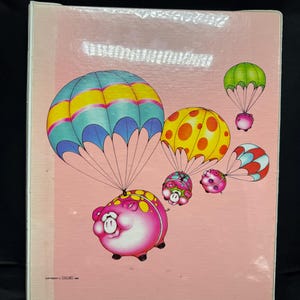 Op de afbeelding: Een roze achtergrond met cartoonvarkens met parachutes in verschillende kleuren. De varkens hebben gele stippen en lachen. De parachutes zijn blauw, geel, rood en groen. Het is een vintage illustratie.