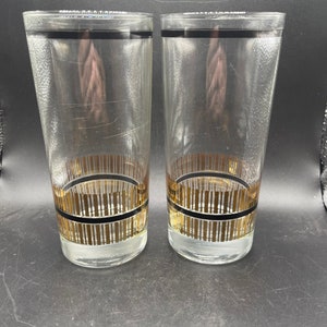 May include: Two clear glass highball glasses with black and gold bands around the middle.