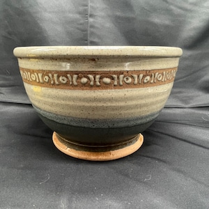 May include: A large, gray ceramic bowl with a brown rim and a decorative pattern. The bowl has a wide base and is perfect for serving salads, fruit, or other dishes.