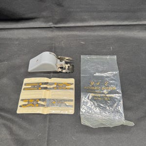 May include: An assortment of sewing machine attachments, including a gray automatic zigzagger, a set of yellow and black guides, and a clear plastic bag with text that reads "Y.S.Z. AUTOMATIC ZIGZAGGER".