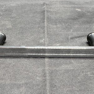 May include: A silver-colored, curved metal handle with two black cylindrical grips. The handle is straight with rounded ends and a slight curve. The grips are positioned at each end of the handle.