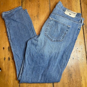 May include: A pair of blue denim jeans with the True Religion brand name and logo on the back pocket.