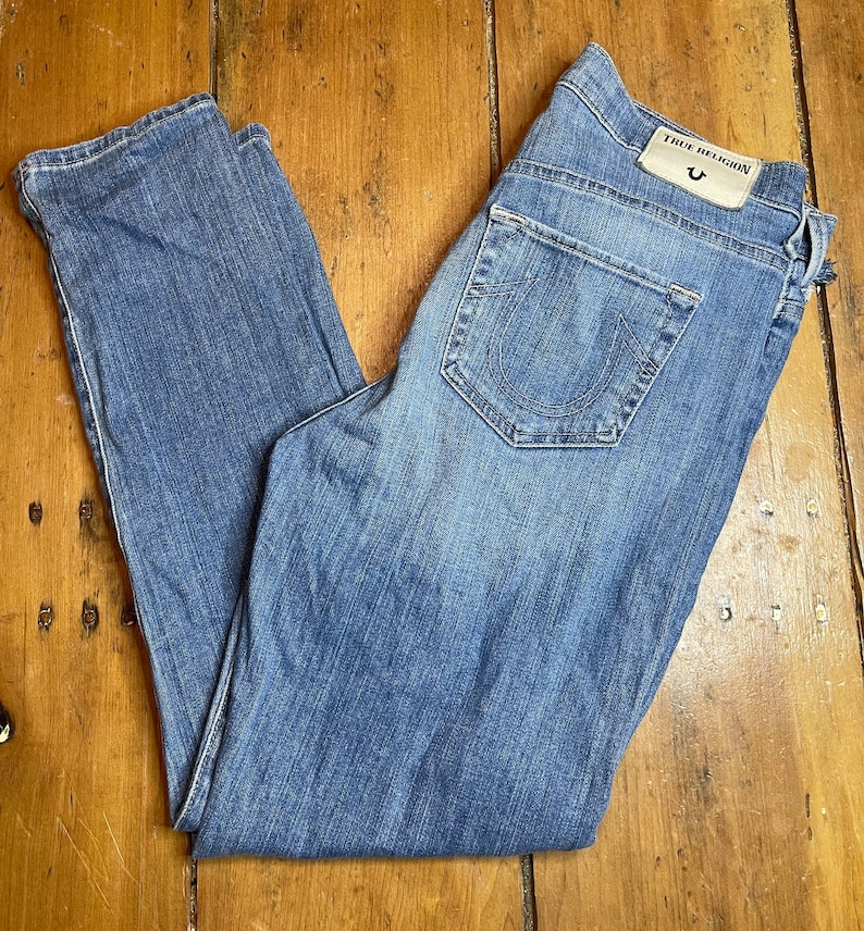 May include: A pair of blue denim jeans with the True Religion brand name and logo on the back pocket.