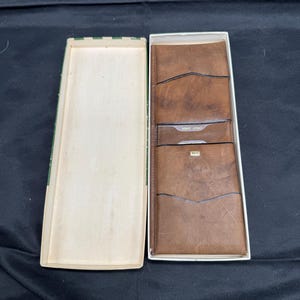 May include: A brown leather wallet with several card slots, displayed in an open rectangular box. The wallet is a rich brown colour, and the box has a green and white striped design on the edges.