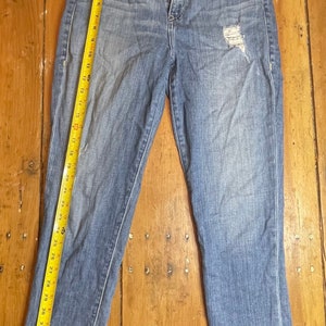 May include: A pair of light blue denim jeans with a distressed detail on the right leg. The jeans have a straight leg fit and a mid-rise waist.