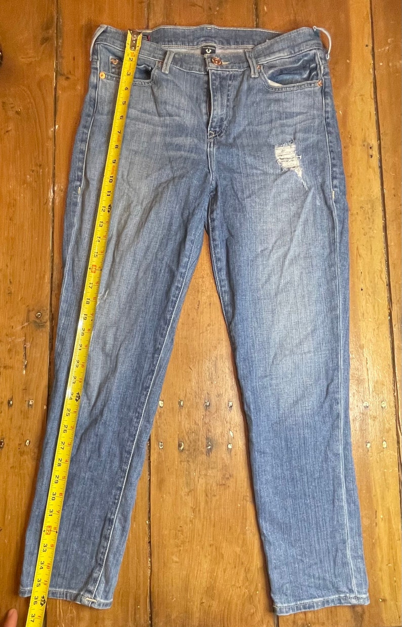 May include: A pair of light blue denim jeans with a distressed detail on the right leg. The jeans have a straight leg fit and a mid-rise waist.