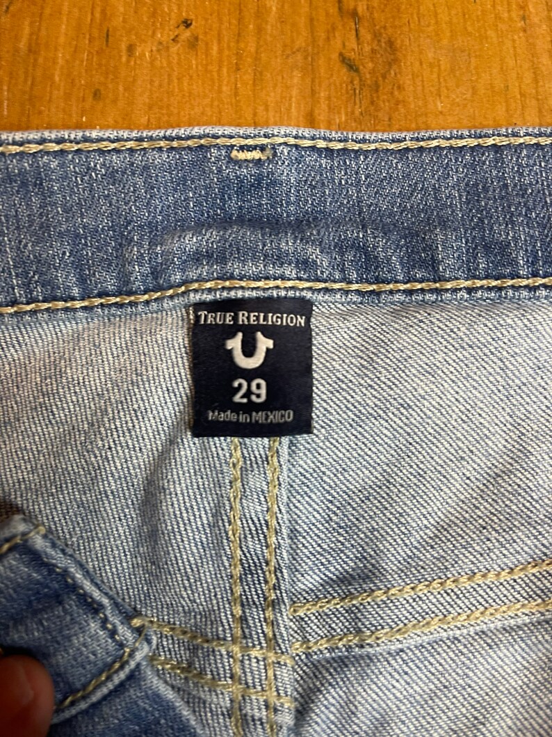 May include: A blue denim jean label with the text "True Religion" and a stylized "U" logo. The label also includes the size "29" and the text "Made in Mexico."