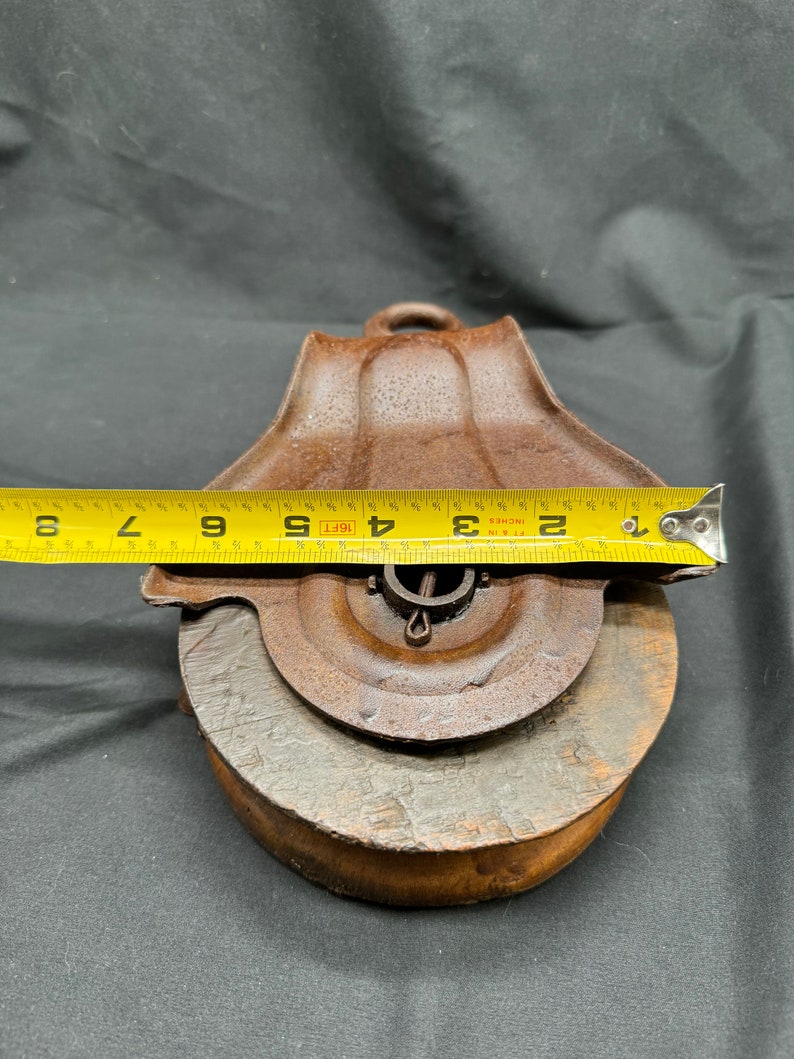 May include: A rusty metal pulley with a wooden wheel, measuring 4 1/2 inches in diameter. The pulley has a metal hook and a metal pin for attaching a rope.