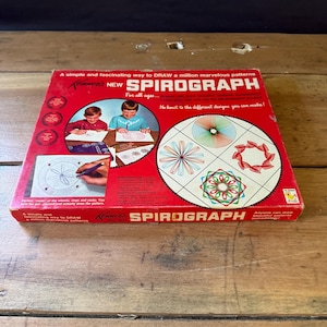 May include: A red, white and blue box for the Spirograph drawing toy. The box shows two children drawing with the Spirograph. The text on the box reads "A simple and fascinating way to DRAW a million marvelous patterns. Kenner NEW SPIROGRAPH For all ages... No limit to the different designs you can make! Kenner No. 401 SPIROGRAPH Anyone can draw beautiful patterns immediately!"