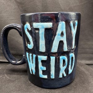Peut inclure: Une tasse en céramique bleu foncé avec un glaçage bleu clair. La tasse porte l'inscription "Stay Weird" en lettres en relief.