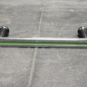 May include: A silver-colored metal handle with a green stripe and two black knobs. The handle has a curved design and is likely for a cabinet or drawer.