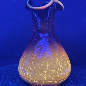 May include: A decorative glass vase with a crackle pattern. The vase transitions from a yellow base to a dark orange and purple top. The rim has a gold trim. The vase is on a dark blue surface.