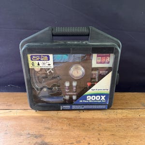 May include: A black plastic carrying case containing a 28-piece microscope set. The set includes a microscope, slides, and other accessories. The case has a handle and the text "Explore The World Around You" and "900X 28 Piece Microscope Set".