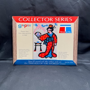 May include: A box for a SnaPics Collector Series set featuring a woman in a red and blue kimono holding a fan. The box is brown with a red and white border. The text on the box reads "Collector Series" and "SnaPics Plastic tiles that make pictures a snap!" The box also includes the text "You'll want all the other sets in the "FRIENDS OF THE WORLD" series" and "Set No. 222".