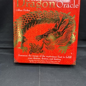 May include: A red box with gold lettering and a gold dragon illustration. The text reads "The Dragon Oracle" by Gillian Stokes. The box also includes text about fulfilling dreams and destiny with Chinese divination tools.
