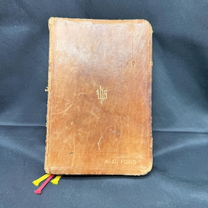 May include: A brown leather-bound book with gold lettering. The book has a bookmark with red and yellow tassels. The title on the cover is "A.C. Ford".